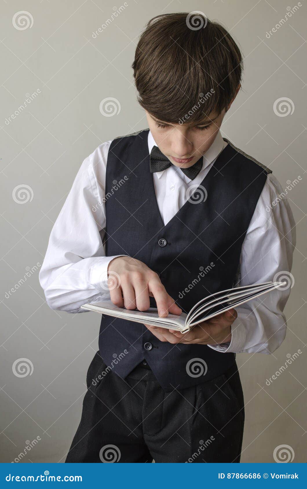 Мальчик подростка в белой рубашке и жилете с черной бабочкой читает ...