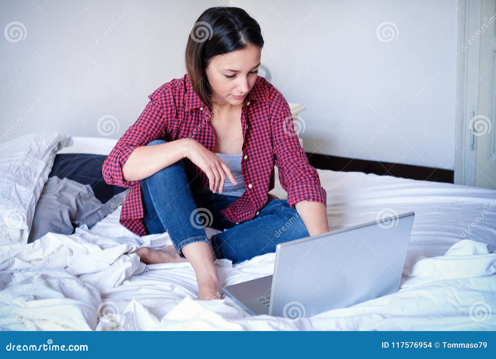 Маленькая девочка используя компьютер и занимающся серфингом сеть сидя на кровати. Видео маленькой девочки наблюдая течь на компьтер-книжке сидя на кровати
