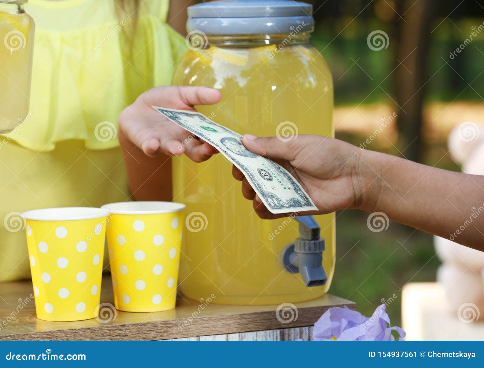 Маленькая девочка продавая естественный лимонад к Афро-американскому мальчику в парке, крупном плане (