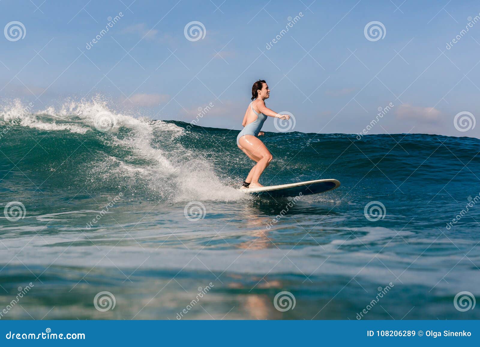 Молодая женщина в ярком бикини занимаясь серфингом на доске в океане. Девушка серфера на изумительной голубой волне, острове Бали