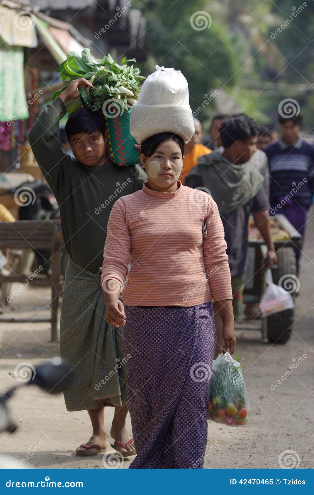 BAGAN, МЬЯНМА 4-ОЕ ЯНВАРЯ: Неопознанная бирманская женщина нося рис на умерших в рынке на bagan, Мьянме 4-ого января 2011 носить головой бирманские традиционные на Мьянме