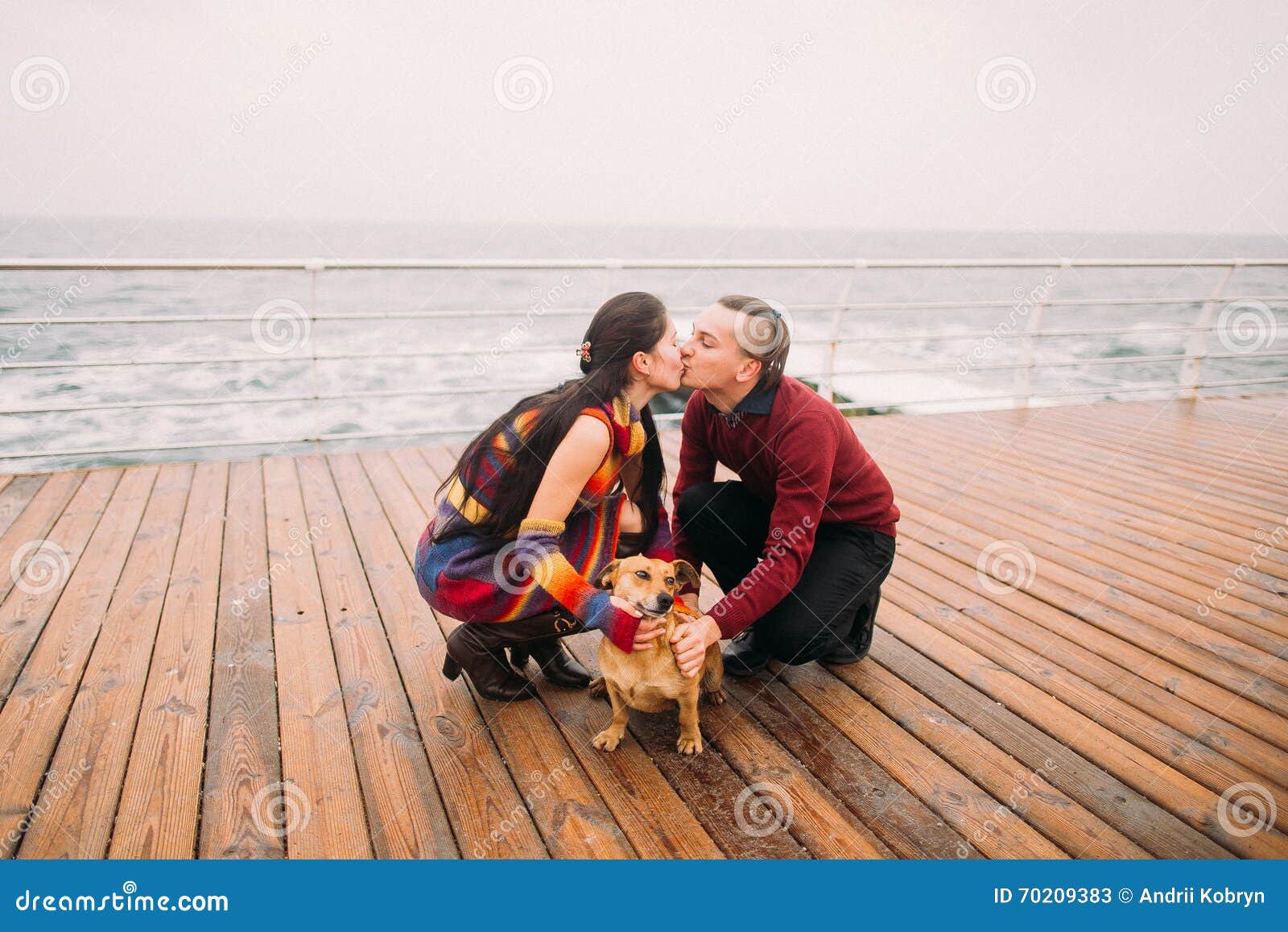 Один другого молодых счастливых пар целуя и играть с собакой на ненастной койке в осени солнце моря луча fiords предпосылки