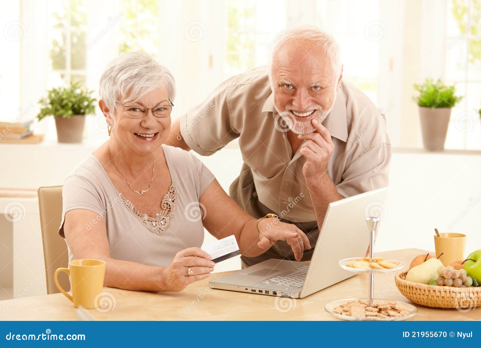 Портрет счастливой старой покупкы пар он-лайн. Портрет счастливых старых пар используя кредитную карточку и портативный компьютер, котор нужно ходить по магазинам он-лайн, женщины указывая на экран.