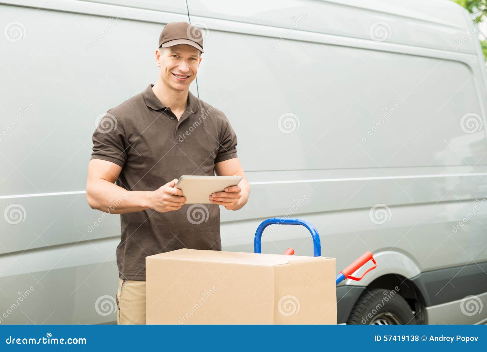 Работник доставляющий покупки на дом с таблеткой и коробками цифров. Молодой счастливый работник доставляющий покупки на дом с таблеткой и картонными коробками цифров
