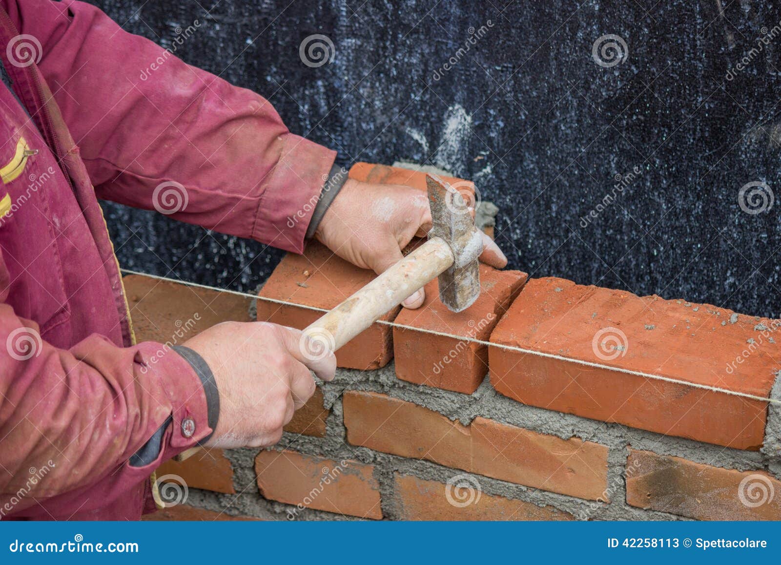Работник построителя при молоток каменщика кладя твердый кирпич глины .