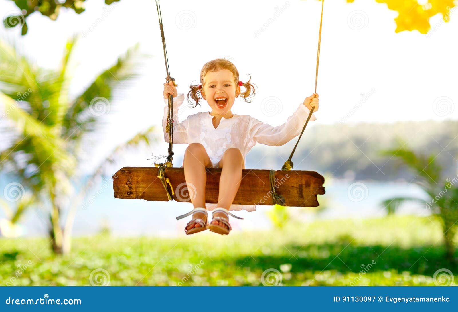 Счастливая девушка ребенка отбрасывая на качании на пляже в лете. Счастливая девушка ребенка смеясь над и отбрасывая на качании на пляже около океана в лете