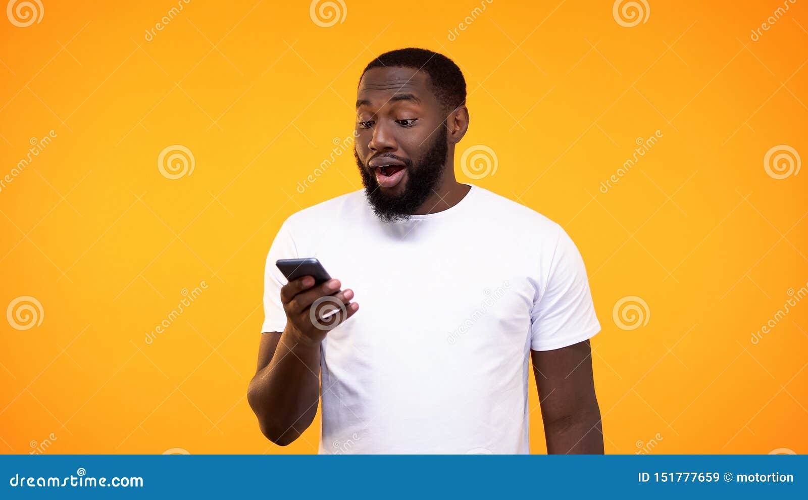 Удивленный чернокожий человек используя применение смартфона против желтой предпосылки, фото запаса