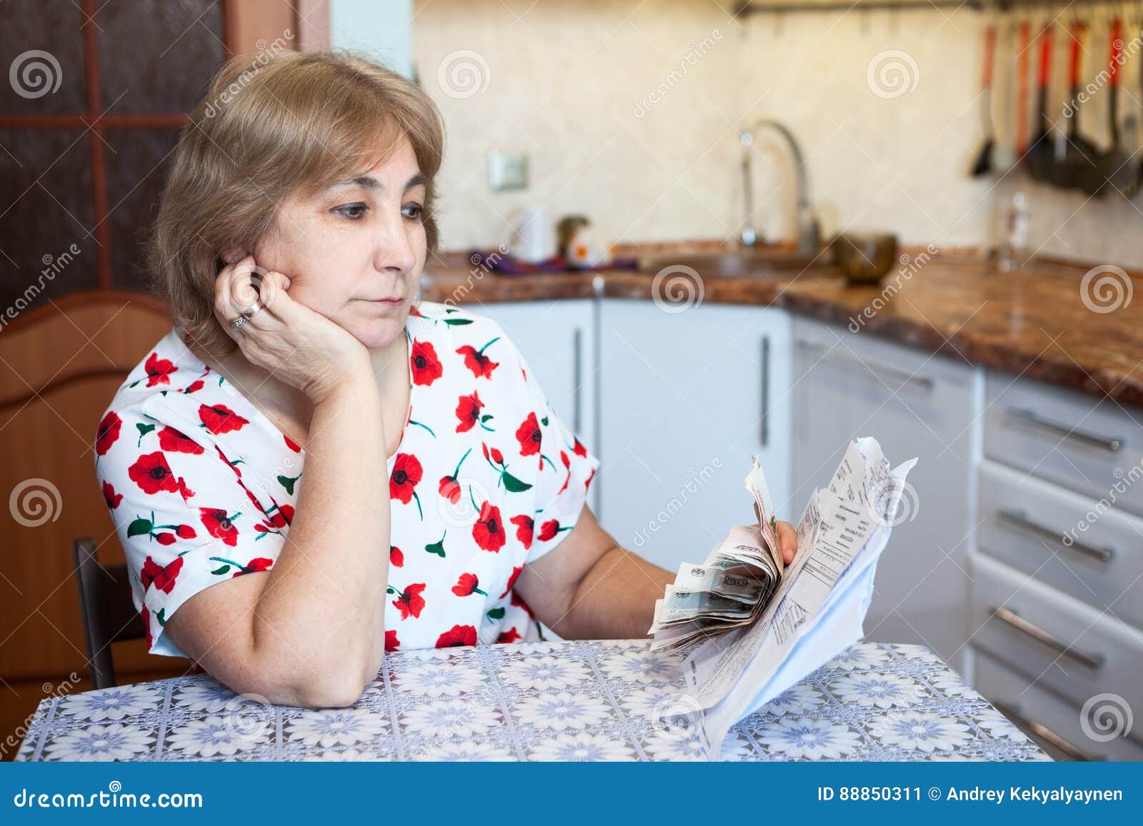 Унылая кавказская старшая женщина смотря счеты с деньгами наличных денег в руке пока сидящ на кухне