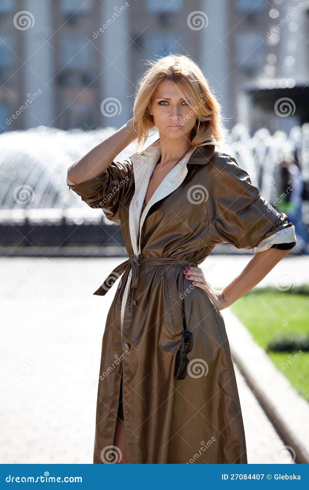 Фасонируйте женщину в пальто осени около фонтана. Портрет женщины около фонтана в глянцеватом пальто осени