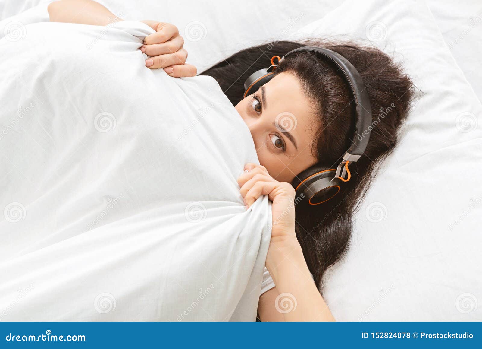 Ослабьте время Шаловливая девушка в наушниках пряча под одеялом, слушая музыку в наушниках, открытый космос