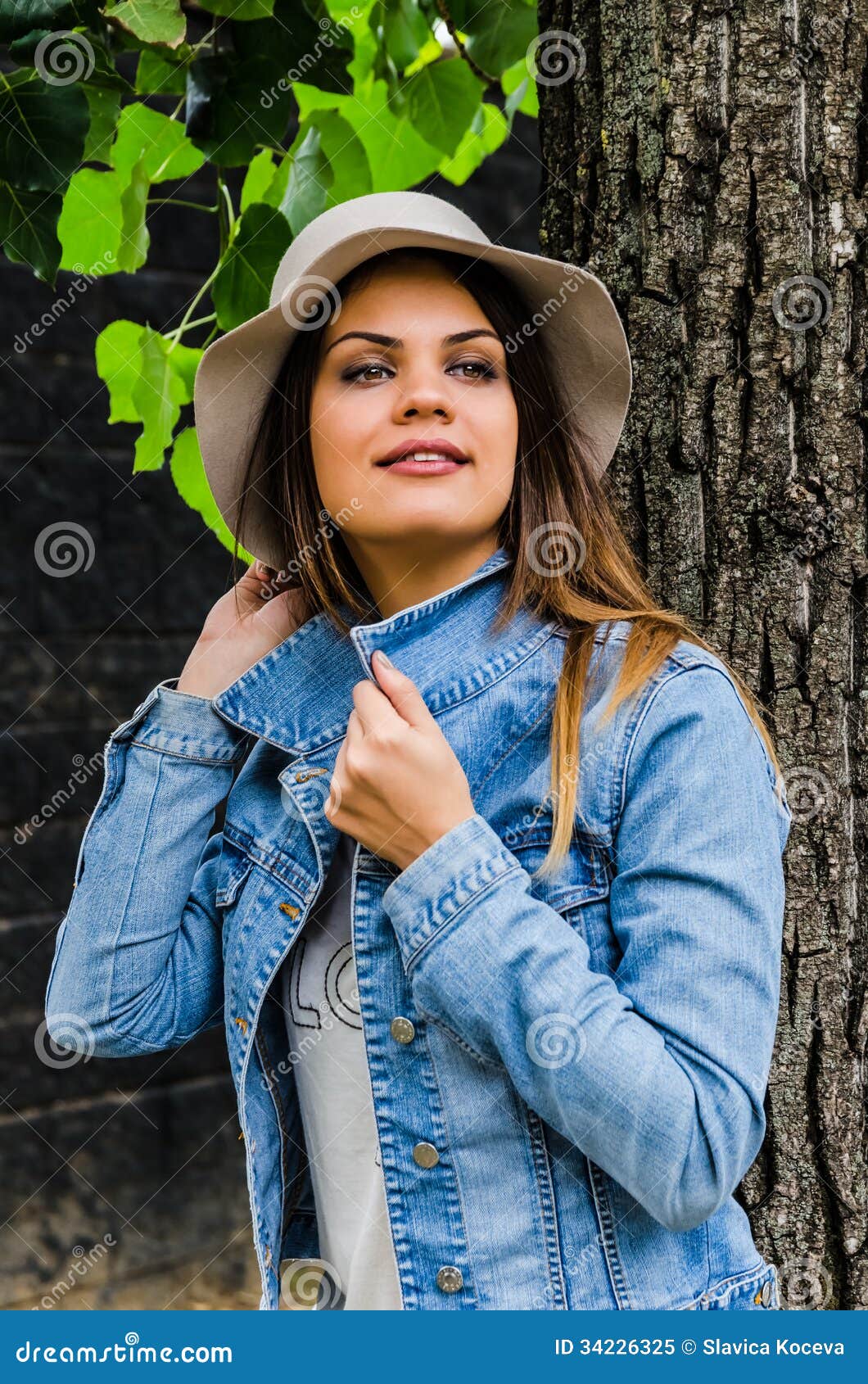 Эмоции. Это фото молодой красивой девушки при шляпа представляя рядом с деревом.