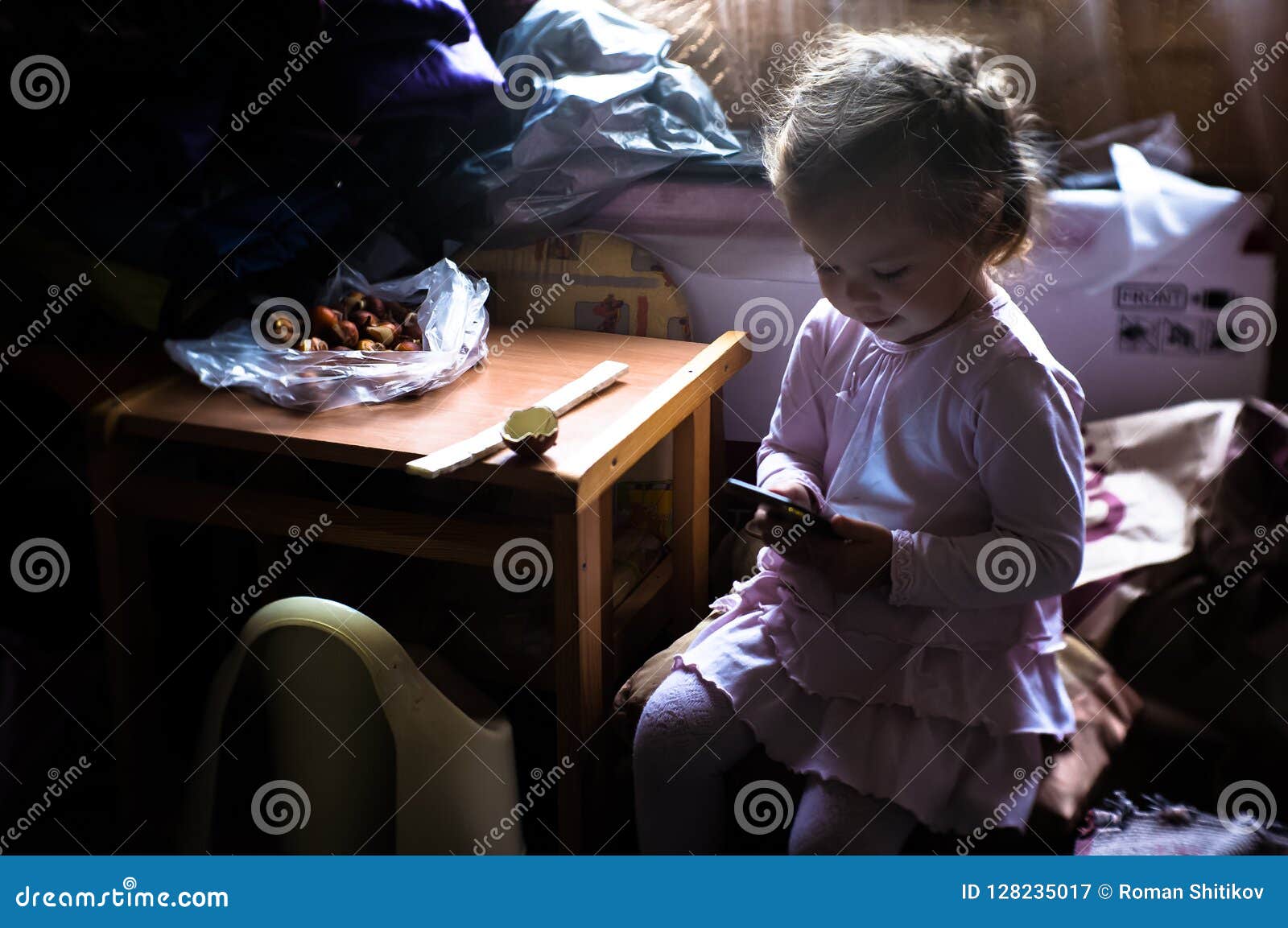 一个小女孩得知互联网通过一个手机. 使用有耳机的快乐的年轻小女孩孩子便携式计算机学习通过网上电子教学系统在黑板背景
