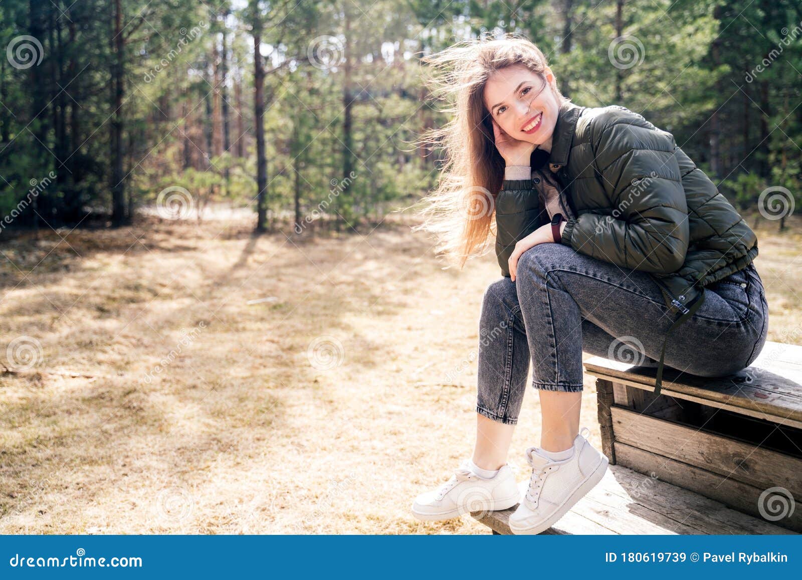 一个快乐的年轻女子坐在森林或公园的木凳上，面带微笑地直视着镜头