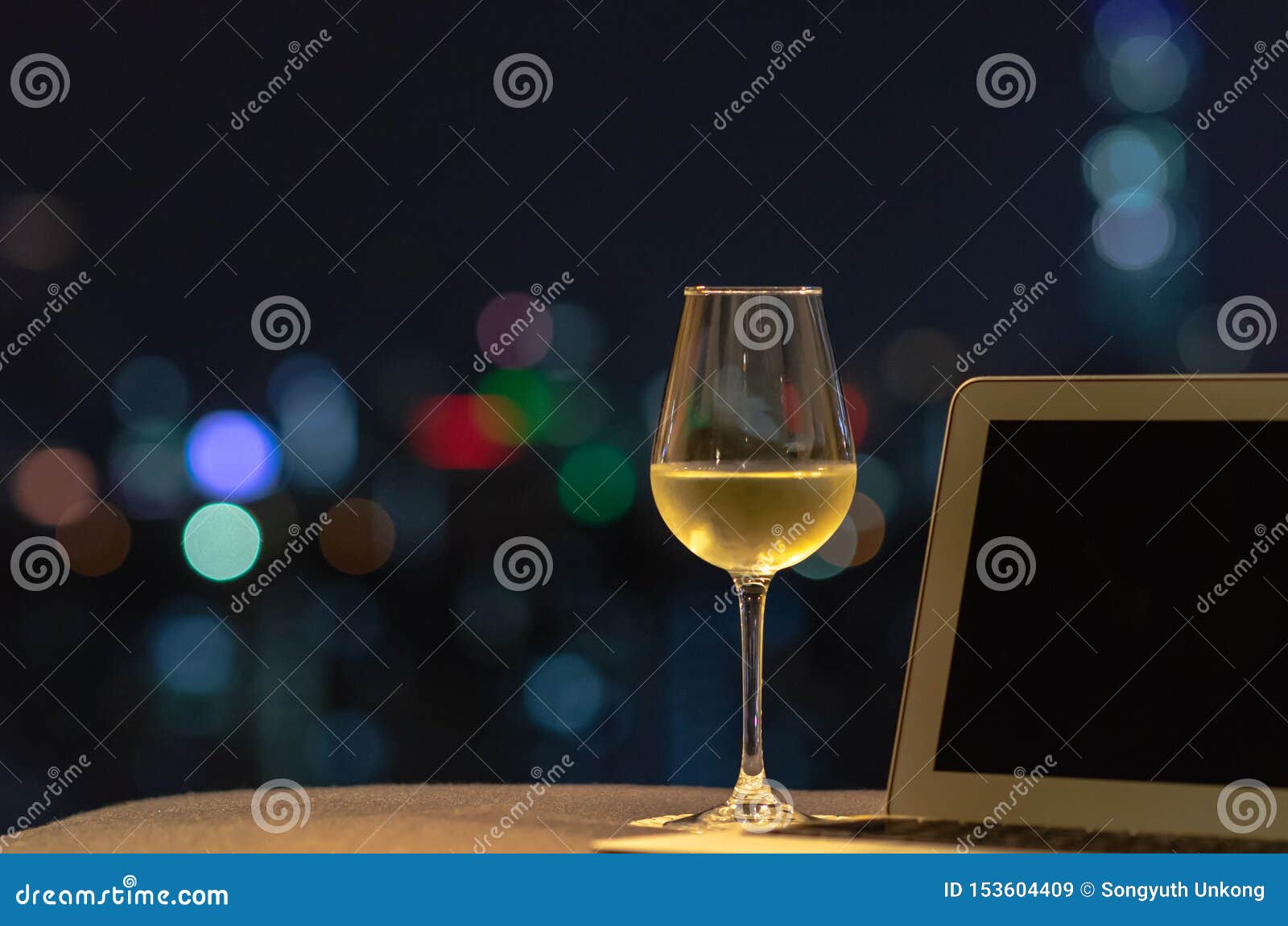 与白酒的一块玻璃投入有手提电脑的沙发有从城市的五颜六色的bokeh光的