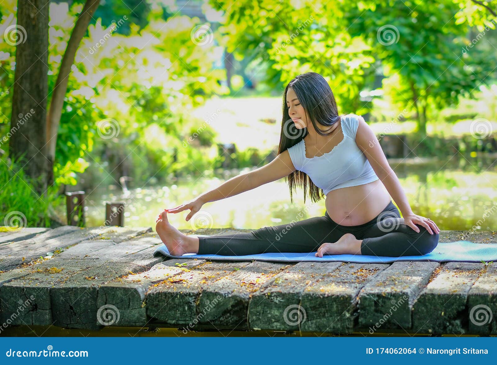 亚洲年轻孕妇坐在花园河边的木桥上练瑜伽的画像库存照片. 图片包括有