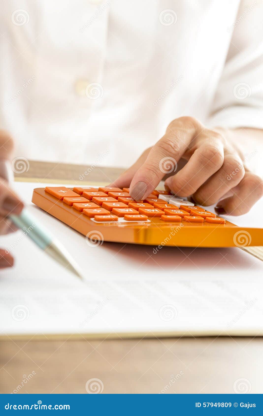使用一个手工计算器的妇女. 使用一个五颜六色的橙色手工计算器在办公室，她坐在她的书桌，她的手看法的关闭的女实业家