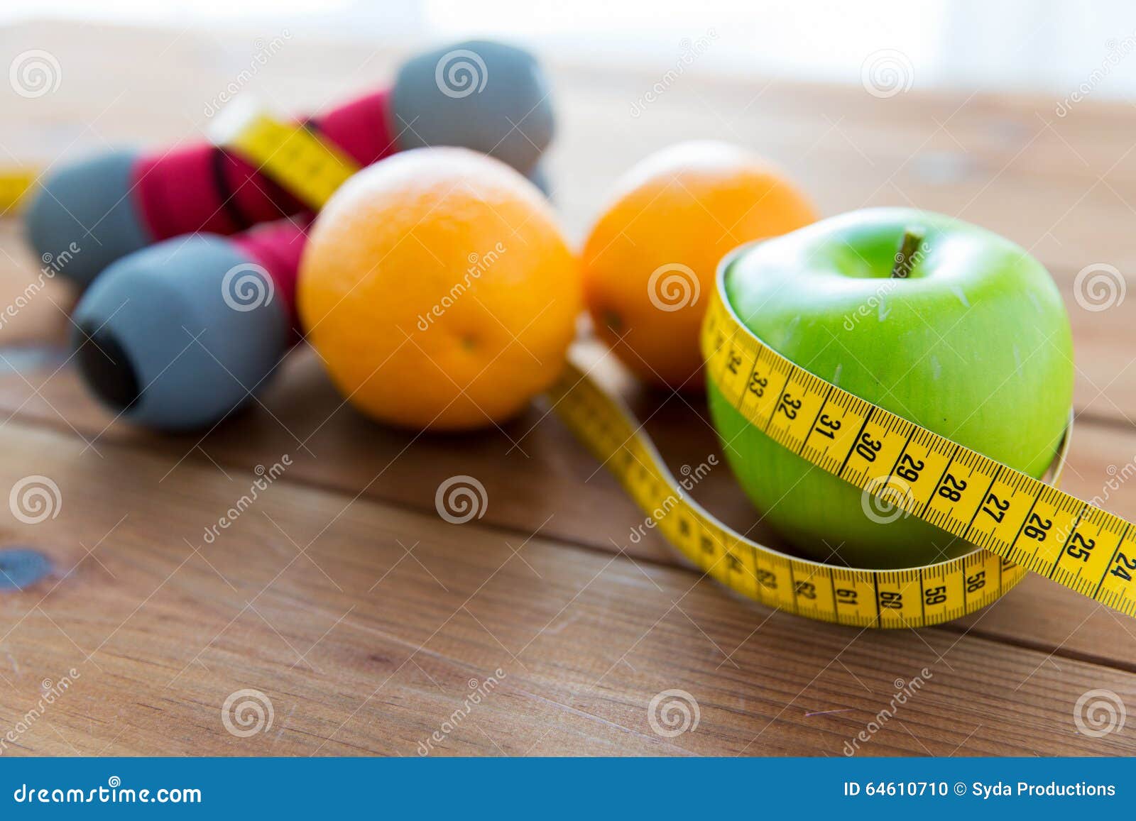 关闭哑铃、果子和测量的磁带. 体育、健身、饮食和对象概念-接近哑铃和绿色苹果用测量包裹的桔子磁带在木桌上