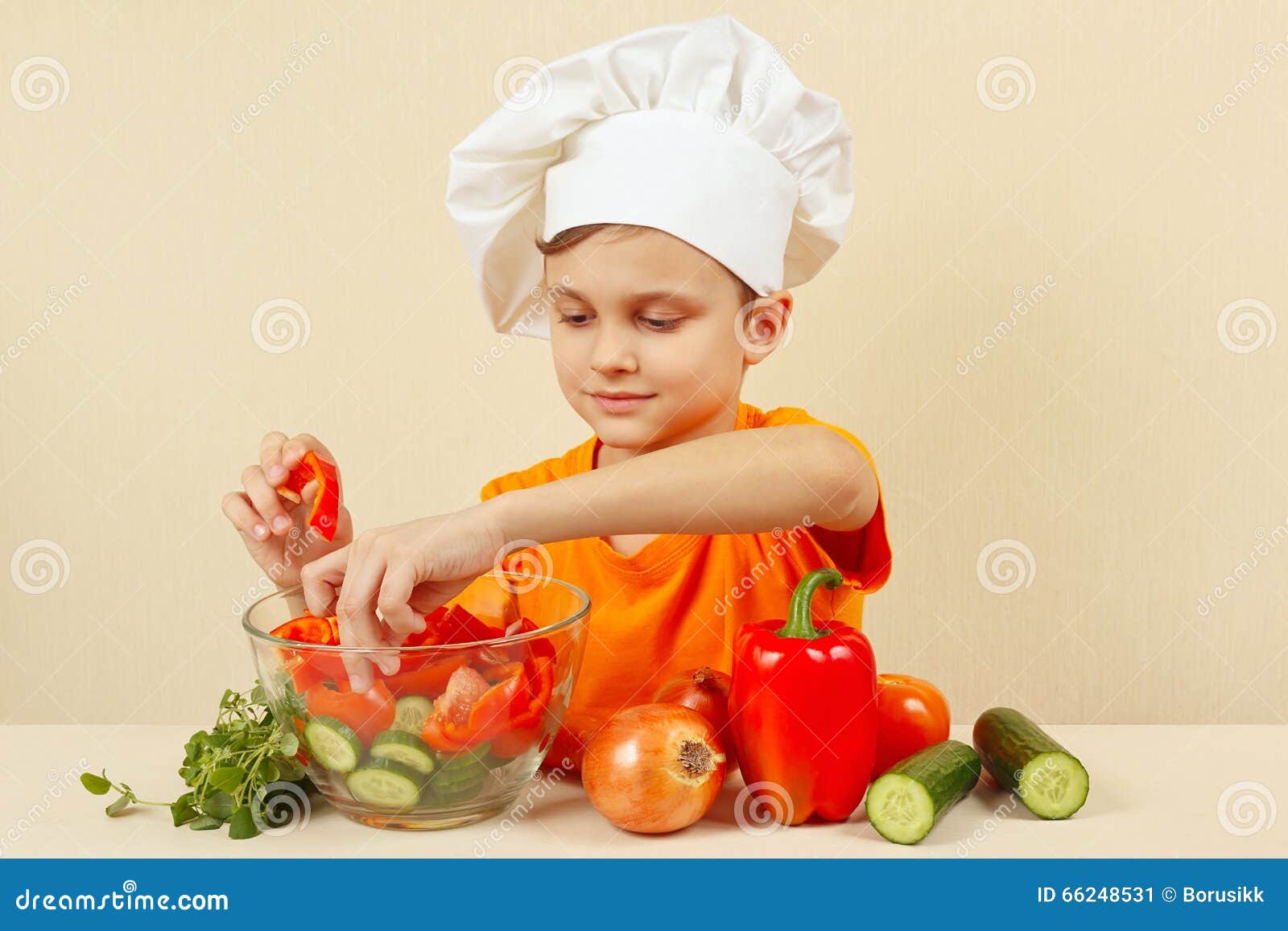 厨师帽子的小男孩在碗投入沙拉的切好的菜