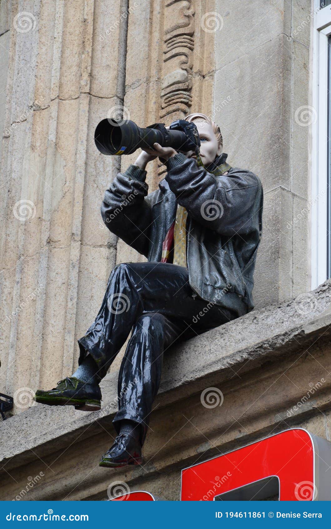古龙广场上一栋建筑的壁架上，坐着一位摄影师的雕像. 德国科隆广场上一栋建筑的壁架上坐着一位摄影师的雕像