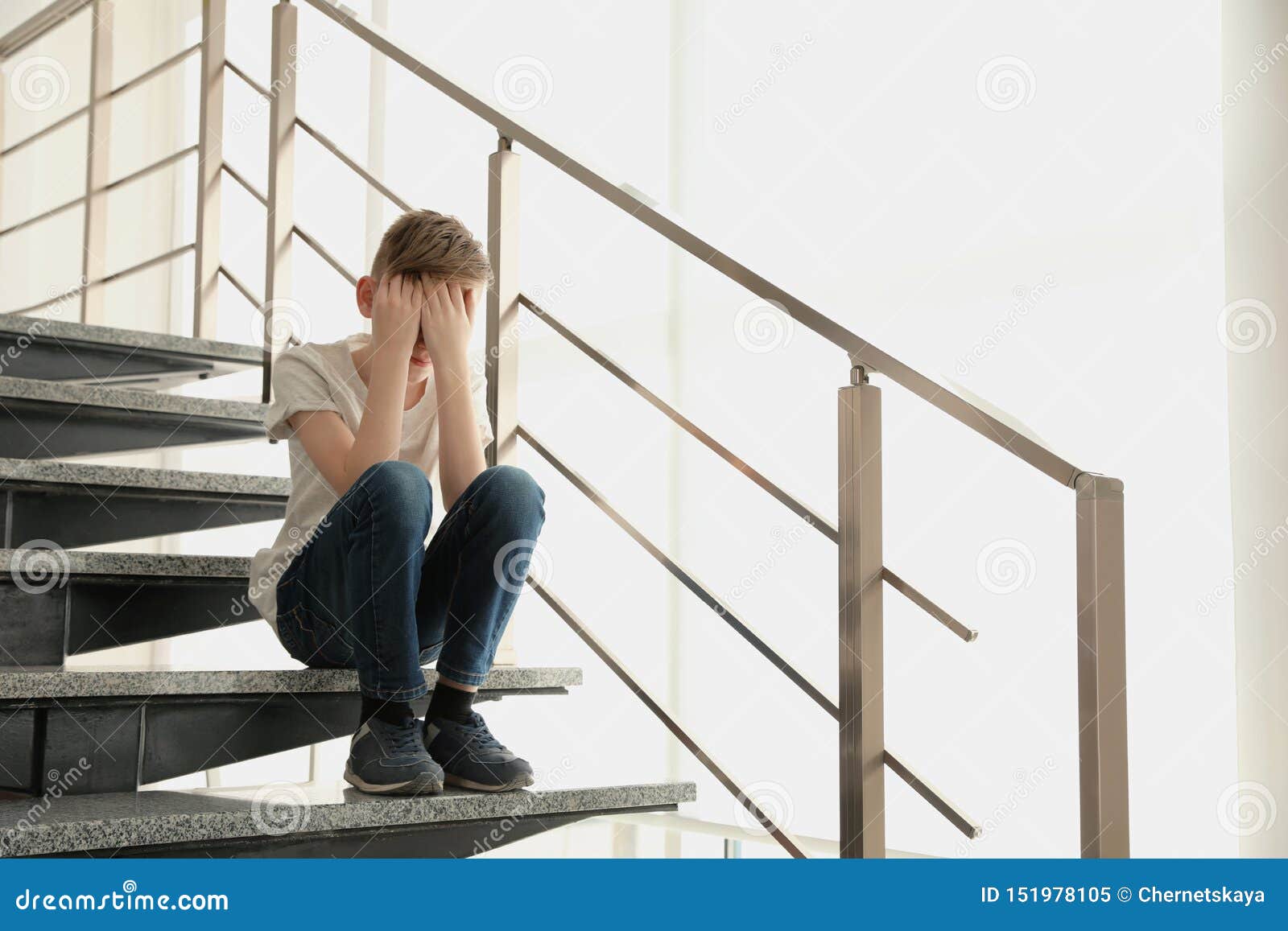 一个男孩痛苦地坐在地板上, 抱着膝盖, 在白色的背景上孤独地哭泣高清摄影大图-千库网