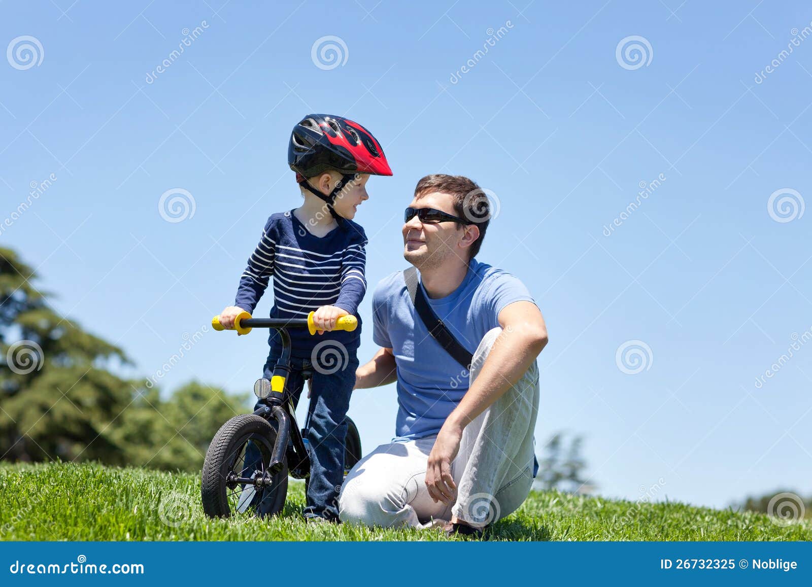 在公园的系列. 有他的儿子的愉快的微笑的父亲平衡自行车的