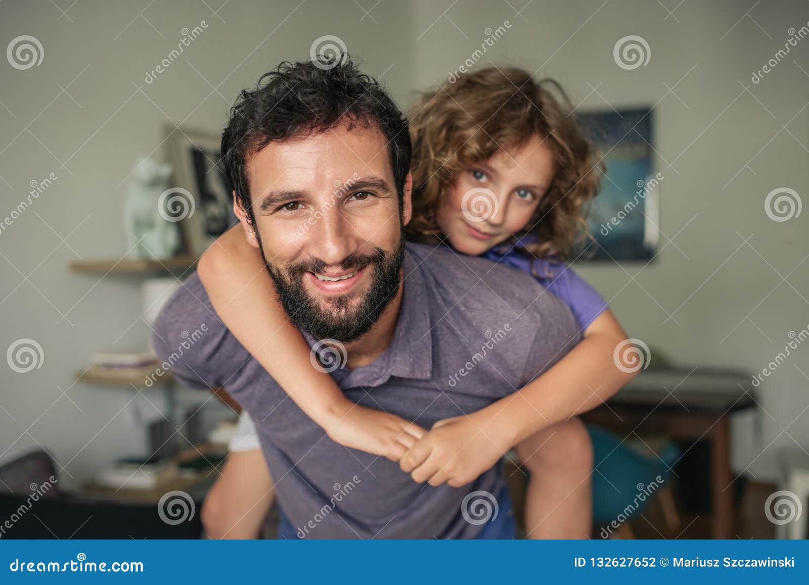 在家给他的儿子肩扛的微笑的爸爸. 给他的年轻儿子肩扛乘驾的微笑的爸爸，当有乐趣时间一起在家时