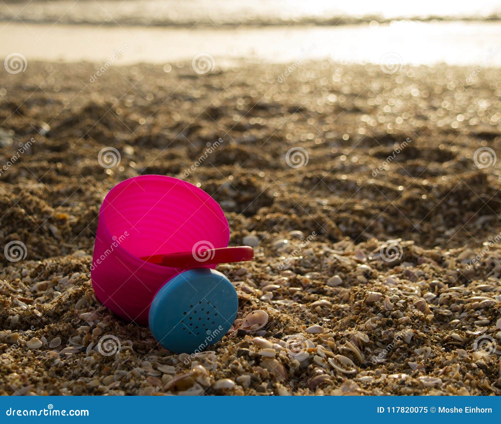 在海滩的一个桃红色桶. 一个桃红色塑料桶和一把红色匙子在海滩