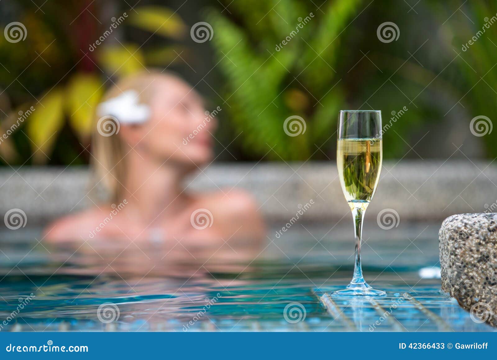 在游泳池附近的香宾在一名美丽的妇女的背景放松
