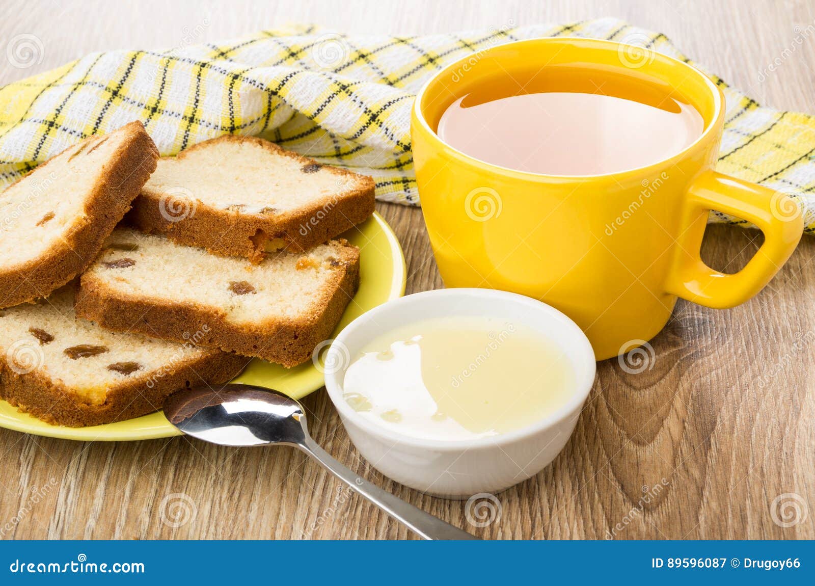 在茶碟，碗的松饼用浓缩牛奶，茶. 松饼用在茶碟、碗用浓缩牛奶，茶和匙子的葡萄干在木桌上