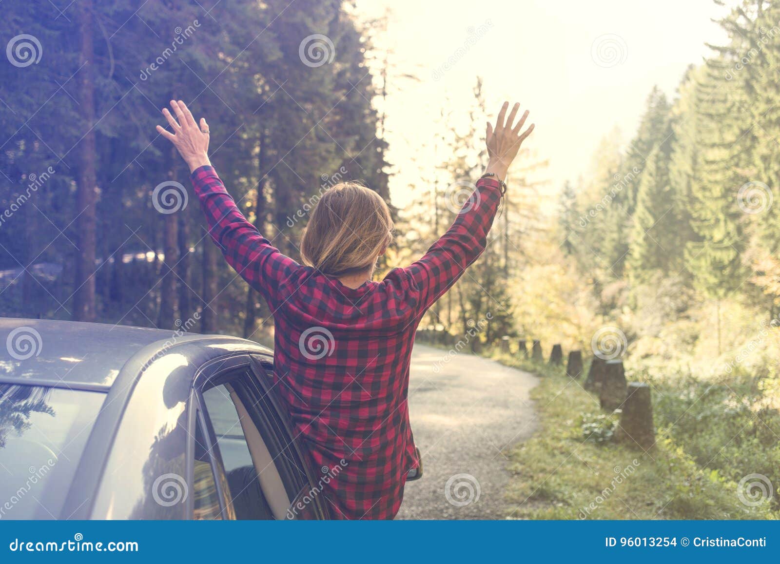 少妇举她的胳膊对倾斜在车窗外面的天空在旅行期间