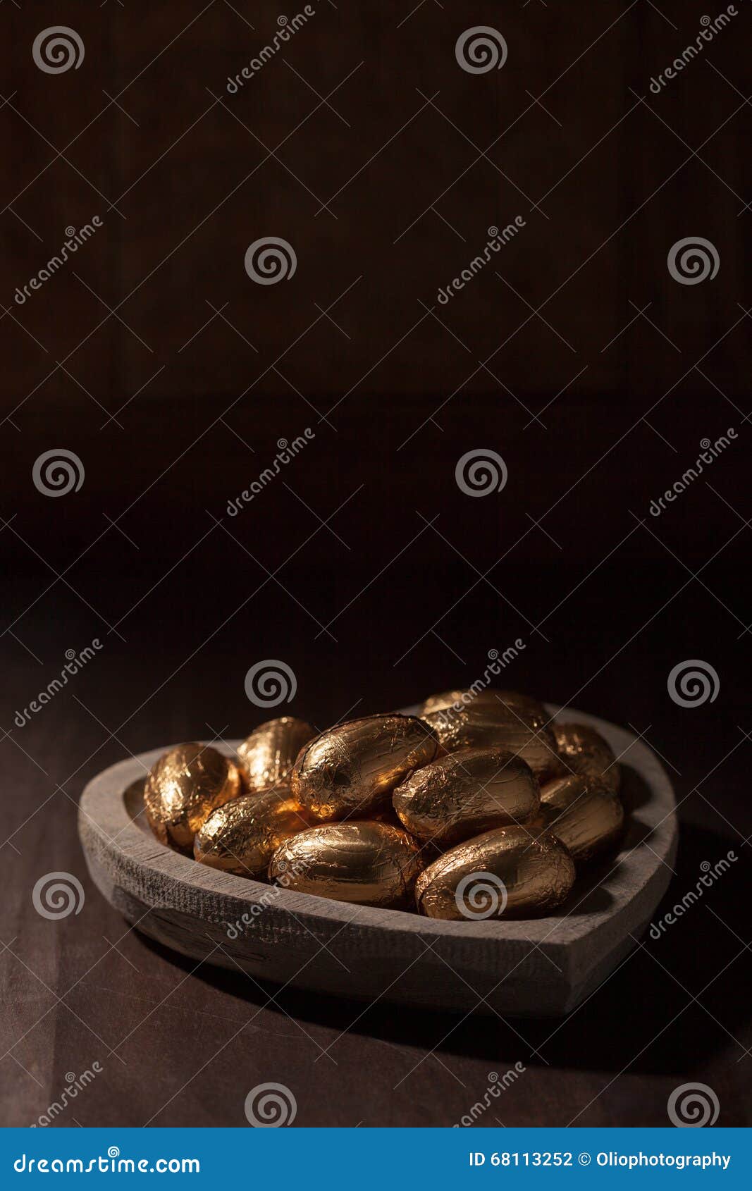 巧克力微型鸡蛋，包裹在金箔. 在金箔的复活节彩蛋，在一个心形的木碗，反对黑暗的背景
