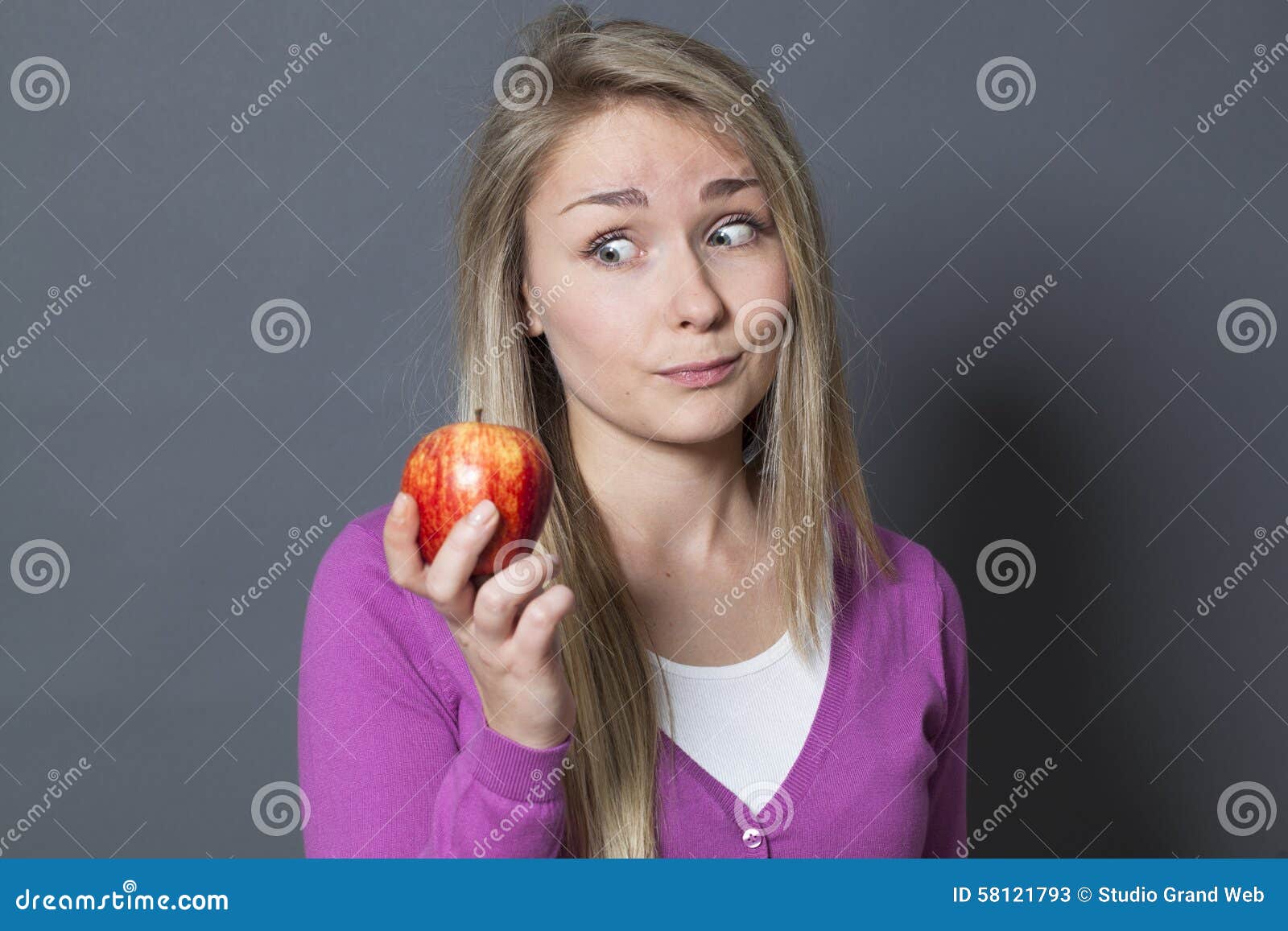 拿着充满欲望的无辜的20s女孩一个开胃苹果. 食物概念-现代雪白和健康胃口的概念的红色苹果给催眠的逗人喜爱的年轻白肤金发的女孩的标志
