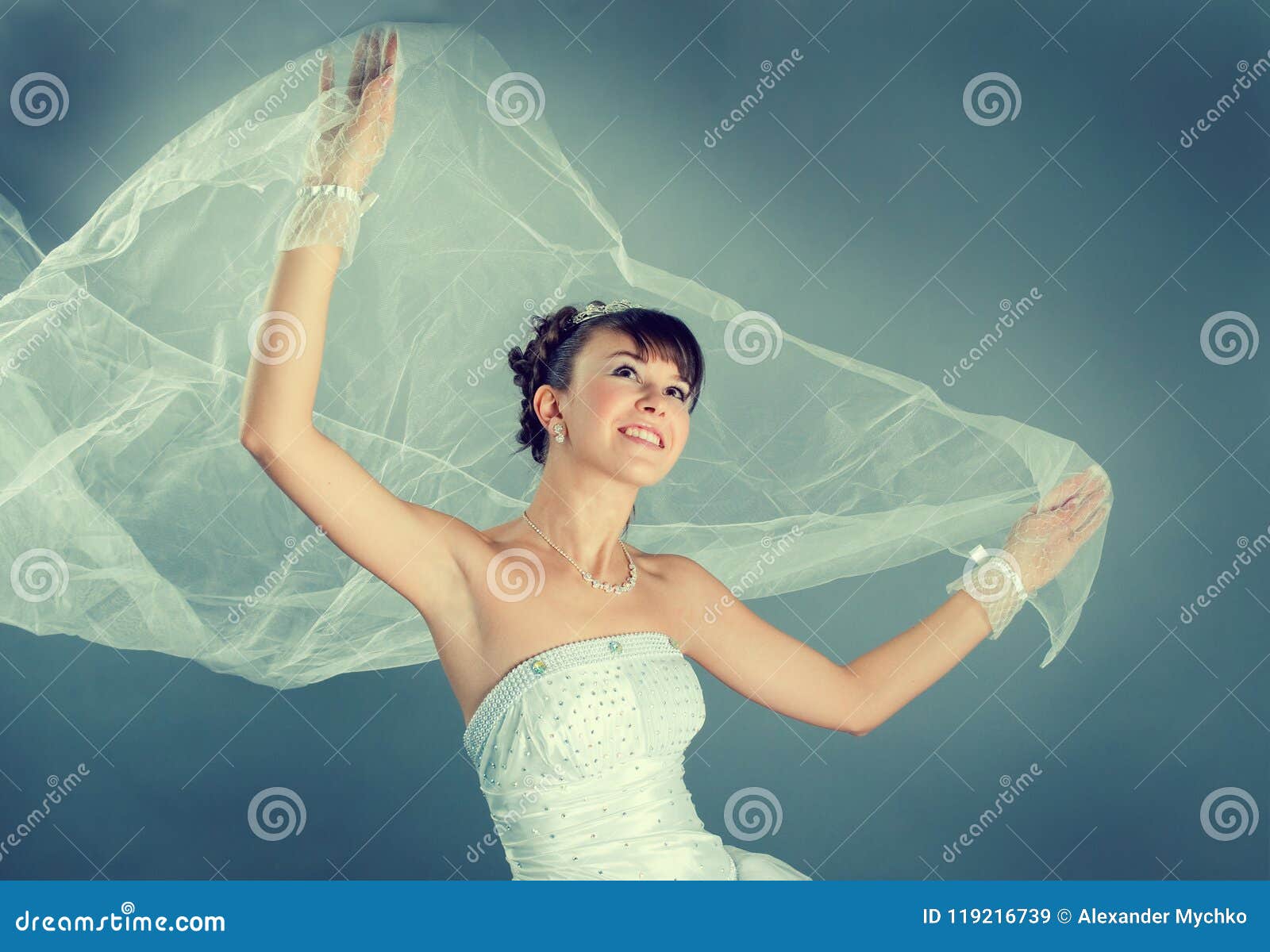 新娘礼服穿戴的高雅婚礼白色. 秀丽年轻新娘在高雅白色婚礼礼服灰色演播室背景中穿戴了
