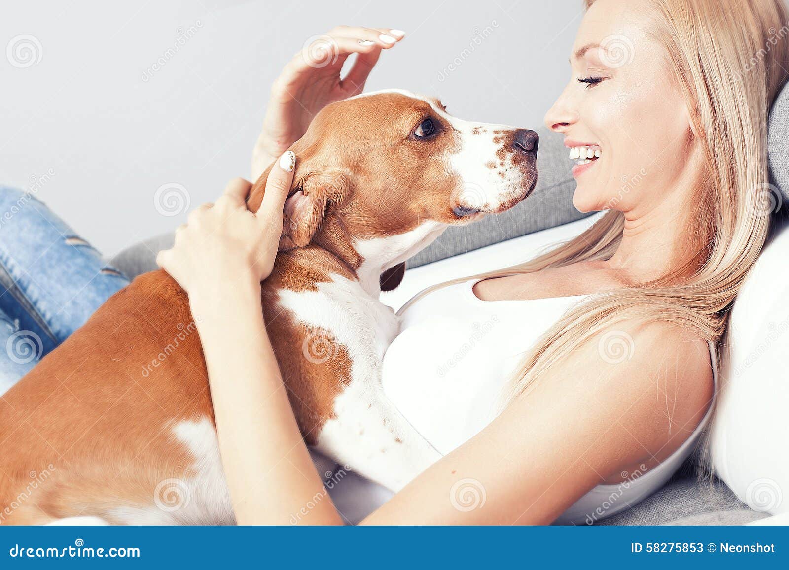 有小猎犬的愉快的白肤金发的女孩. 在家使用与她的狗的美丽的年轻白肤金发的妇女，微笑 幸福