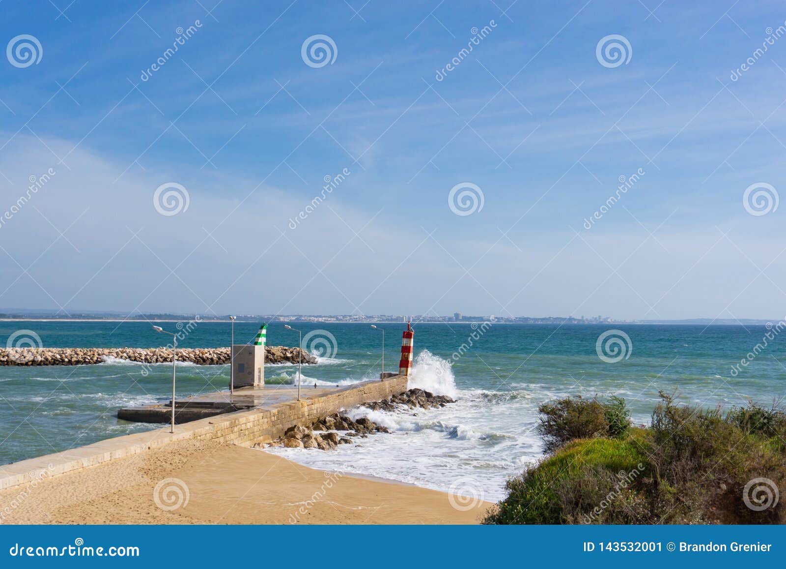 灯塔波浪崩溃拉各斯，葡萄牙. 撞入灯塔的波浪在拉各斯，有城市的葡萄牙距离的