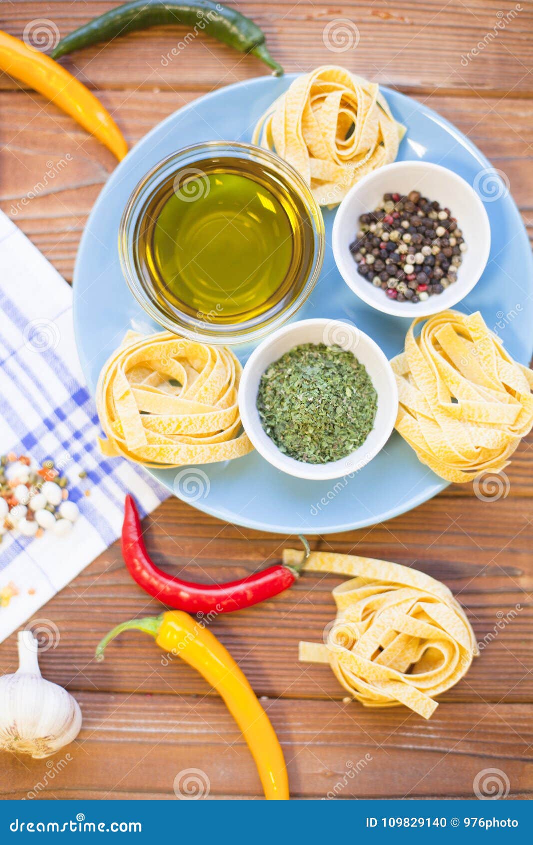 烹调在一张木桌上的成份. 有橄榄油、香料、草本和fetuccini巢的在一块蓝色板材，蕃茄，大蒜，在一张木桌上的辣椒碗与一块白色餐巾，顶视图