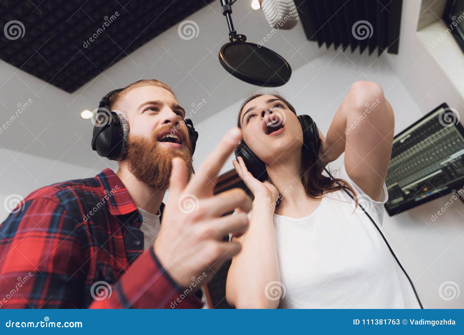 男人和妇女在一间现代录音室唱一首歌曲. 人和妇女在一间现代录音室唱一首歌曲 在人是红色被检查的衬衣，在妇女一件白色T恤杉