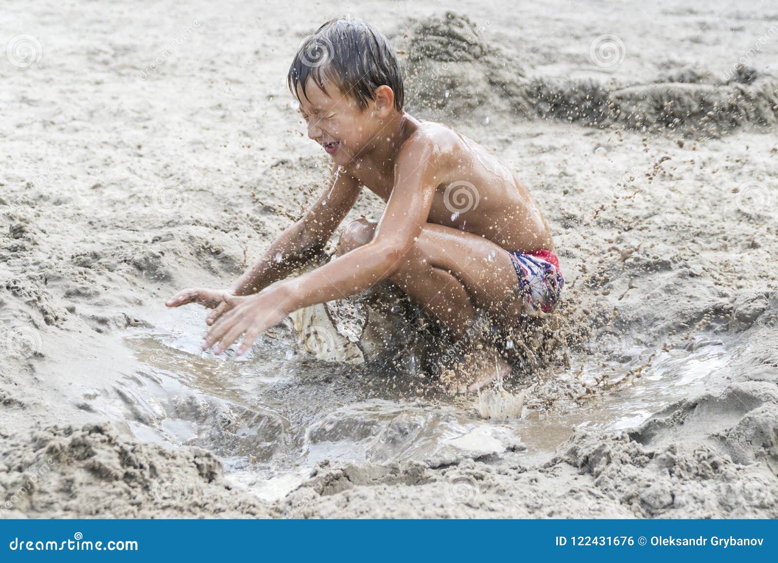 男孩在肮脏的沙子跳. 使用在海滩的小男孩跳跃在湿肮脏的沙子
