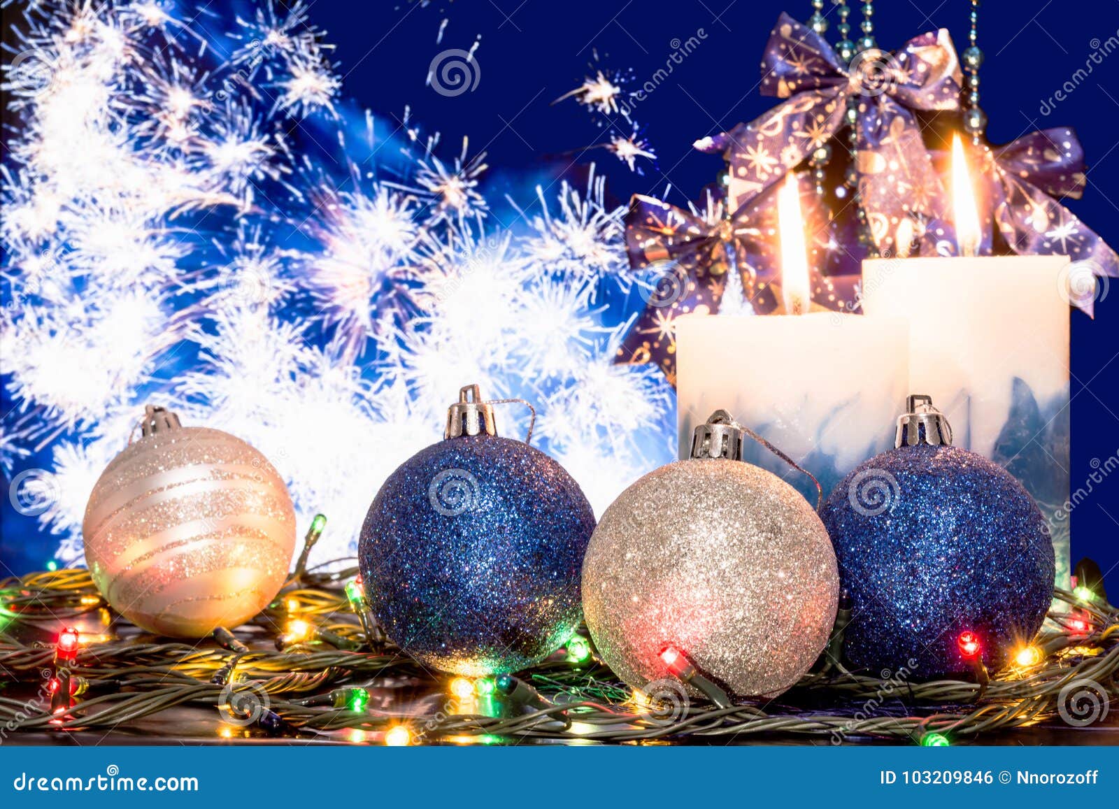 蓝色和银色圣诞节球、一本发光的诗歌选和两个灼烧的蜡烛在欢乐烟花的背景，选择聚焦，圣诞节或新年` s背景