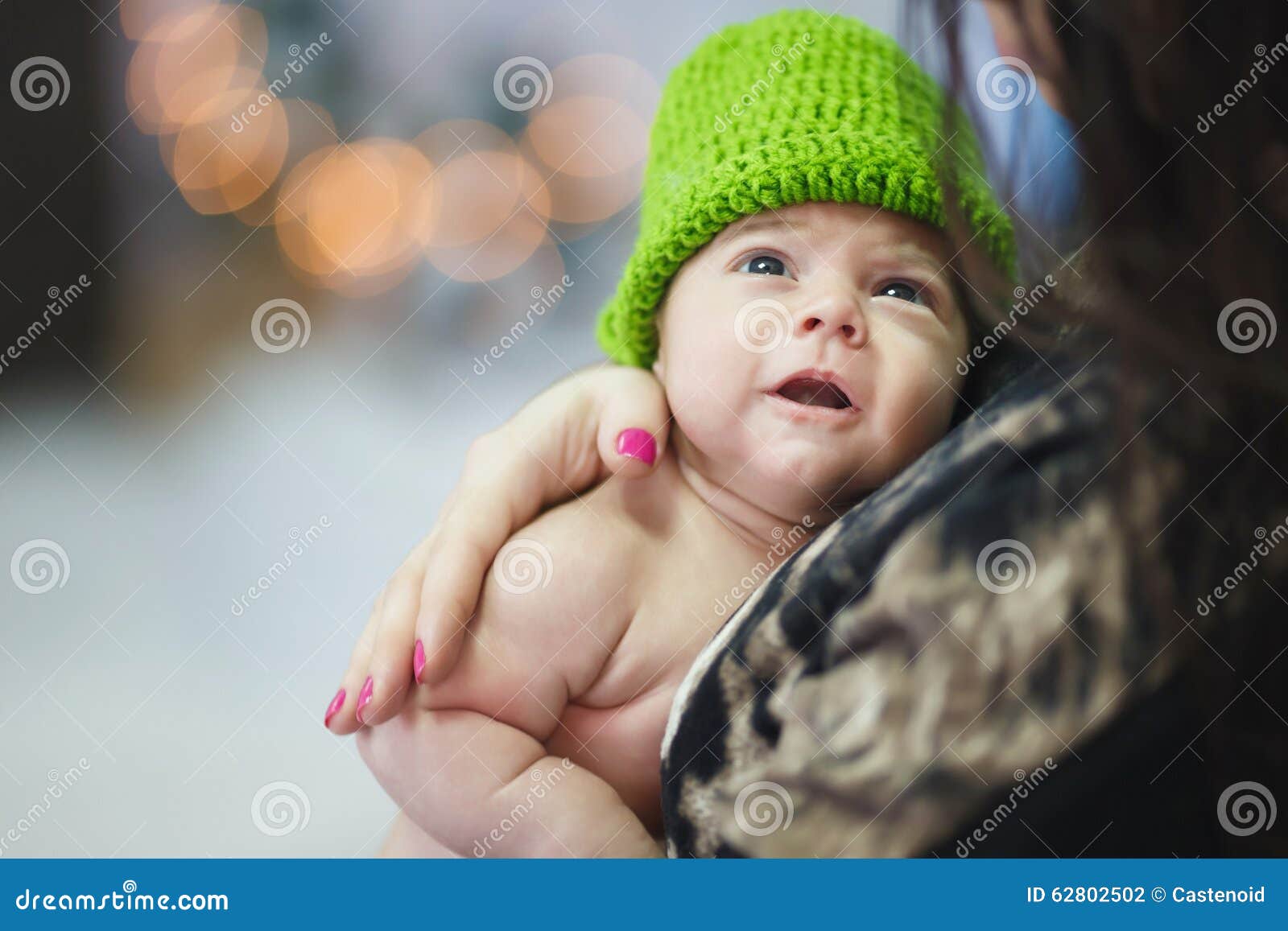 逗人喜爱的婴孩一点. 的婴孩在戴一个绿色帽子的他的母亲的手上